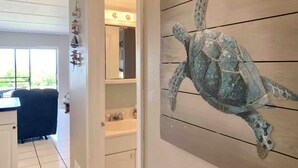 A room with a wooden wall mural of a sea turtle, a white door, and a view of a balcony with a chair. - Cozy Seaside Condo w/ Ocean Views - Pets Allowed! (St. Augustine)