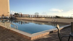 A swimming pool with a tiled deck, a covered area with chairs, and a clear sky. - Cozy Seaside Condo w/ Ocean Views - Pets Allowed! (St. Augustine)