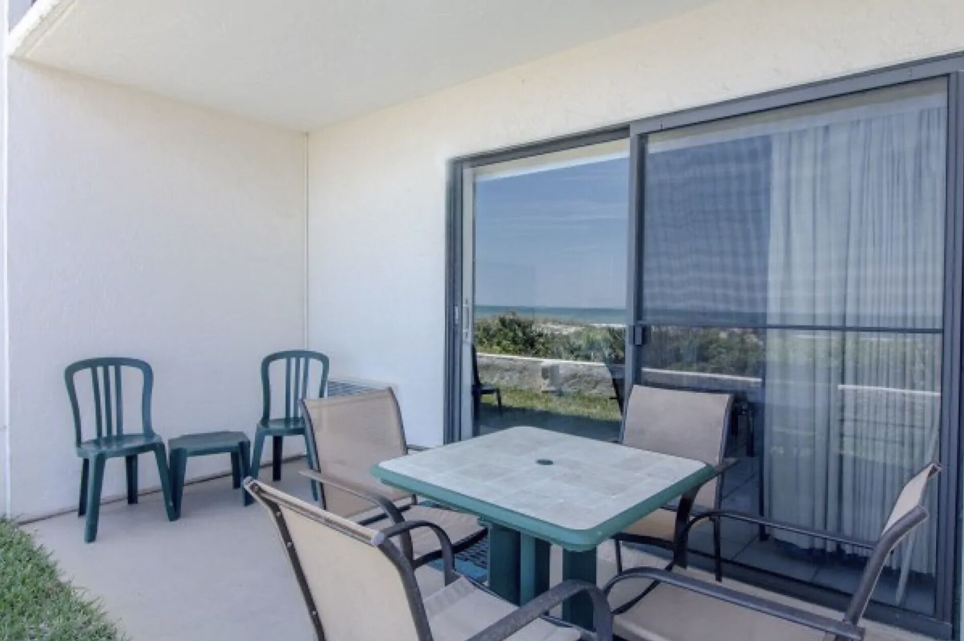 Un balcon avec une table et des chaises, une porte vitrée et une vue sur l’océan.