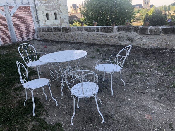 An outdoor seating area with a stone wall, a metal table, and four metal chairs. - Les Abbesses (SAINT-AIGNAN)