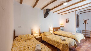 A room with three beds, each with a yellow patterned bedspread and a wooden headboard. There are bedside tables with lamps, a radiator, and a coat rack. - Cortijo Don Simón Cabra by Ruralidays (Córdoba)