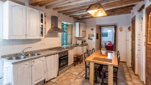A compact kitchen with white cabinets, a granite countertop, a stove, and a dining area with a wooden table and chairs. - Cortijo Don Simón Cabra by Ruralidays (Córdoba)