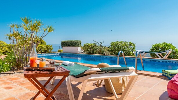 Un espace aménagé au bord de la piscine, avec un fauteuil de relaxation, une table avec une bouteille et des verres, et une vue sur la mer.
