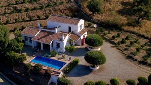 Une maison à deux étages avec une piscine, entourée de jardins aménagés et d’un paysage vallonné.