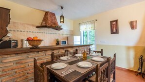 A dining area with a brick wall, a wooden table set for four, and a hanging light fixture.
