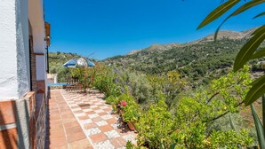 A terrace with a checkered floor, surrounded by greenery and a view of a mountainous landscape.