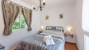 A bedroom with a bed, curtains, a chandelier, bedside tables, and wall art.