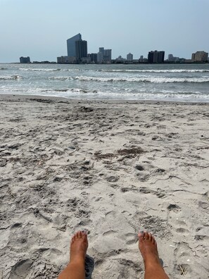 A sandy beach with footprints and seaweed, leading to a city skyline with modern buildings. - Steps to the Beach in Brigantine - Sea Point - Beautiful Pool  (Brigantine)