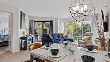 A modern dining area with a glass table set for four, surrounded by a blue sofa and a grey armchair.