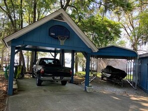 Ein überdachter Parkbereich mit blauem Dach, einem Basketballkorb und einem Grill.