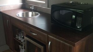 A compact kitchen with a stainless steel sink, a microwave, and wooden cabinets. - Live Free, See Sofia - Premium Room 2 (Chilkiya)