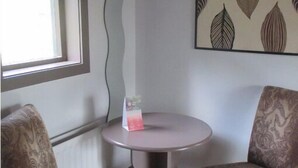 A small room with two patterned chairs, a round table with a single item, a window, and a wall with a leaf-patterned artwork. - Live Free, See Sofia - Premium Room 2 (Chilkiya)