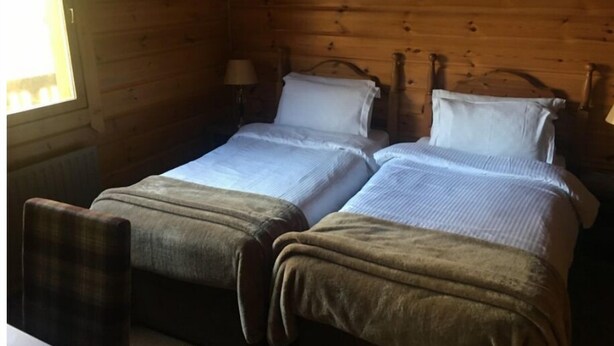 A wooden cabin room with two beds, a chair, and a window. - Live Free, See Sofia - Premium Room 2 (Chilkiya)