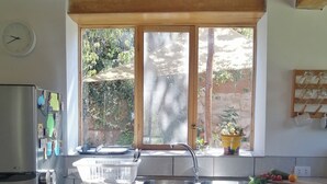 Eine Küche mit Holzausstattung, einem Edelstahlkühlschrank, einem Fenster mit Blick ins Grüne und einem Spülbecken mit Armatur.