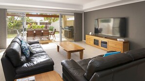 Una sala de estar moderna con un sofá de cuero, una mesa de centro de madera y un televisor de pantalla plana sobre un mueble de madera.