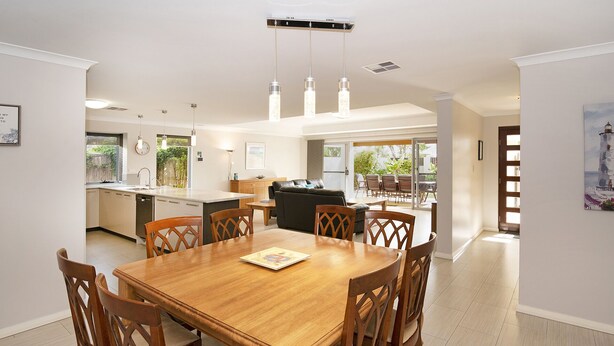 Un comedor amplio con una mesa y sillas de madera, una cocina al fondo y vistas al exterior.