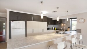 Cocina moderna con una isla central, taburetes de bar, electrodomésticos de acero inoxidable e iluminación colgante.
