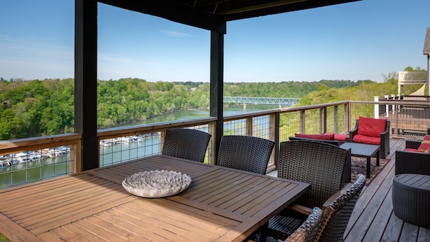 Una terraza de madera con mobiliario de mimbre, con vistas a un río y un puente.