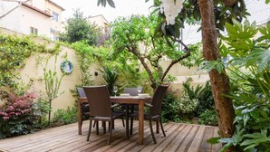 A wooden deck with a table and chairs, surrounded by greenery and a wall with a decorative plate.