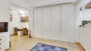 A room with a dining area, a TV, a wardrobe, and a patterned rug.
