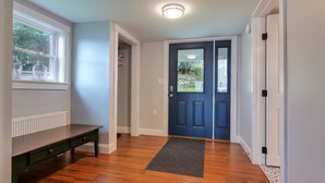 A hallway with a dark blue door, a radiator, a bench, and a window with plants. - Lakefront home, water-view porch (Dedham)