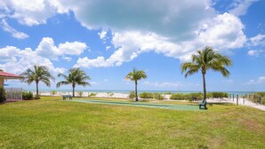 A grassy area with palm trees, a bench, and a view of the beach. - Oceanfront Bonita Beach Condo w/ Pool Access! (Bonita Springs)