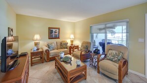 A living room with a sofa, armchairs, a coffee table, and a TV. There are lamps on side tables and a painting on the wall. - Oceanfront Bonita Beach Condo w/ Pool Access! (Bonita Springs)