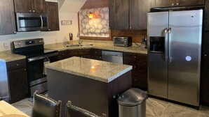 A modern kitchen with dark wooden cabinets, stainless steel appliances, granite countertops, and a built-in island with seating.
