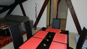 Ein Essbereich mit einem schwarz-roten Tisch, schwarzen Stühlen und einem grauen Sofa in einem Raum mit freiliegenden Holzbalken.