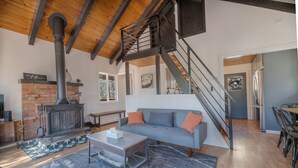 A modern living room with a fireplace, a staircase, and a dining area. - Forest Escape - Secluded Feeling, Forest Views, Fireplace, Deck (Fawnskin)