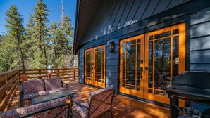 A wooden deck with outdoor furniture, large windows, and a grill. - Forest Escape - Secluded Feeling, Forest Views, Fireplace, Deck (Fawnskin)