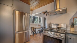 A modern kitchen with stainless steel appliances, a wooden ceiling, and a large window providing natural light. - Forest Escape - Secluded Feeling, Forest Views, Fireplace, Deck (Fawnskin)