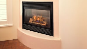 A corner fireplace with a white mantel, a framed picture above it, and a brick floor.