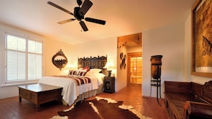 A bedroom with a bed, a wooden bench, a cowhide rug, a ceiling fan, and a rustic wall decor.