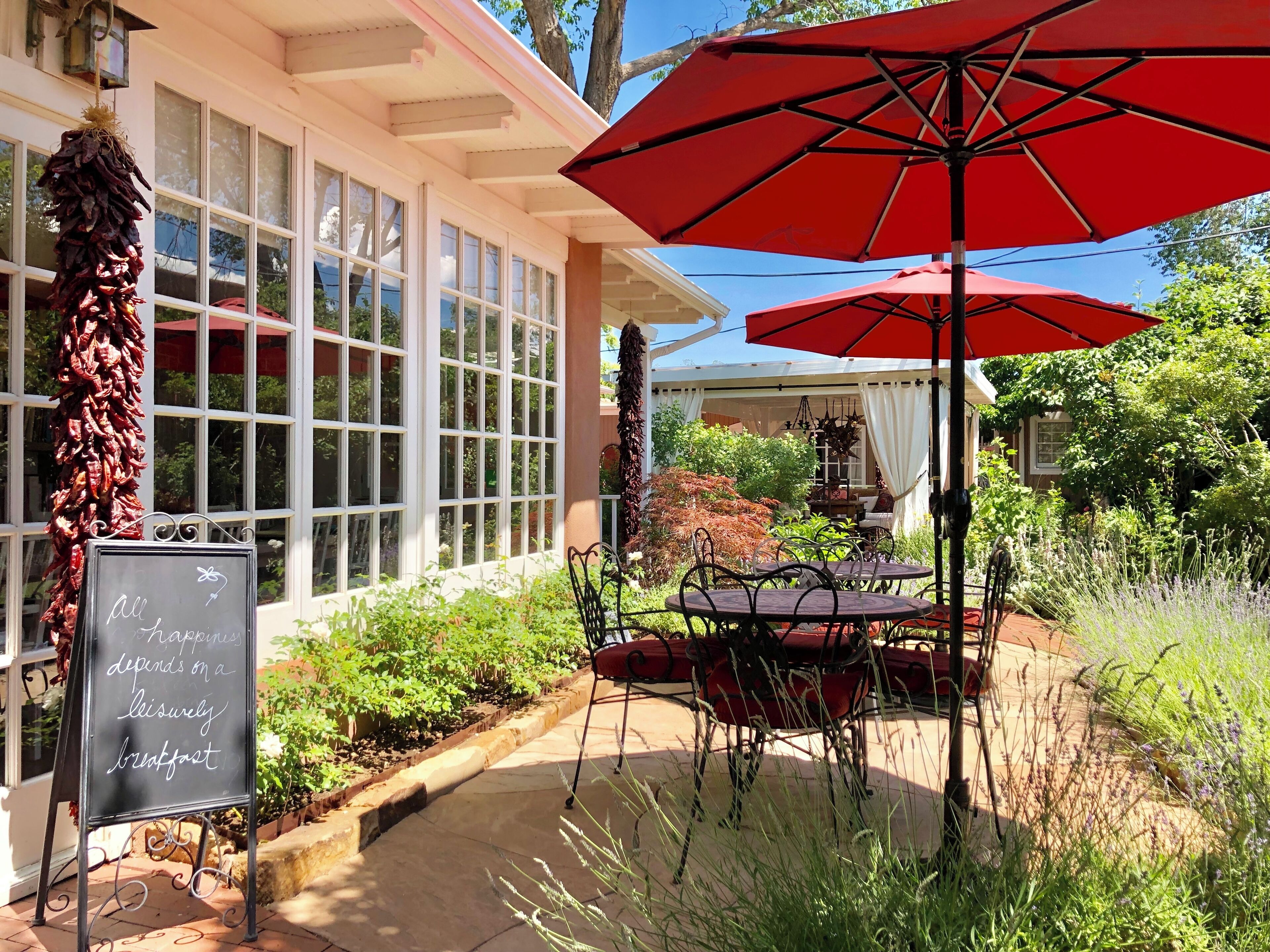 An outdoor seating area with red umbrellas, a chalkboard sign, and a hanging chili pepper display.
