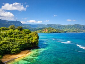 Una playa con aguas turquesas cristalinas, exuberante vegetación y montañas al fondo.