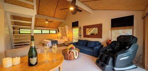 Ein gemütliches Wohnzimmer mit Bett, Massagesessel, Couchtisch mit Blumen und einer Champagnerflasche.