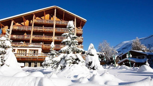Un edificio de madera de varios pisos con balcones, rodeado de árboles cubiertos de nieve y montañas al fondo.