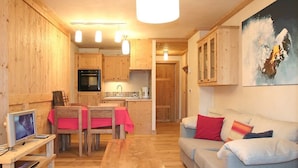 Una sala de estar acogedora, con muebles de madera, un comedor y una cocina al fondo.