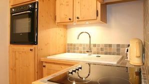 Una cocina con gabinetes de madera, un horno negro, un lavamanos con grifo y una cafetera.