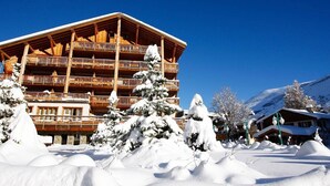 A multi-story wooden building with balconies, surrounded by snow-covered trees and a mountainous backdrop.