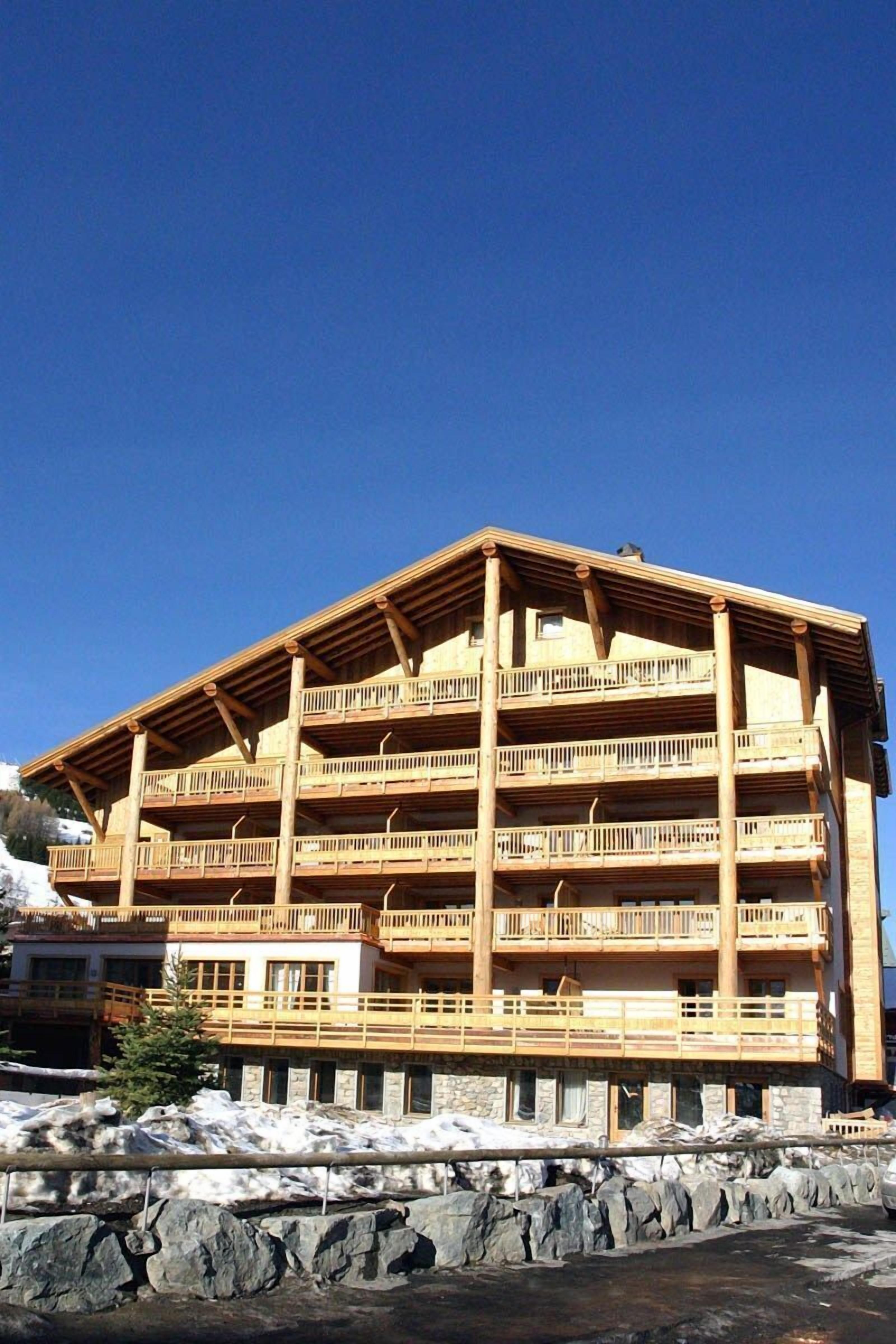 Un edificio de madera de varios pisos con balcones, probablemente un hotel o una posada, con base de piedra y un cielo azul despejado al fondo.