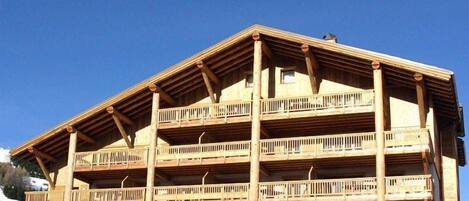Un edificio de madera de varios pisos con balcones, probablemente un hotel o una posada, con base de piedra y un cielo azul despejado al fondo.