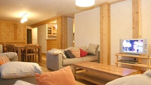 A cozy living room with a sofa, a coffee table, and a television. There is a wooden dining table with chairs.