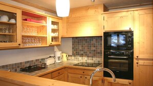 A kitchen with wooden cabinets, a black oven, a tiled backsplash, and a stainless steel sink.