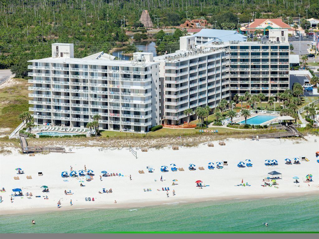 A beachfront hotel with multiple floors, a pool, and beach umbrellas.