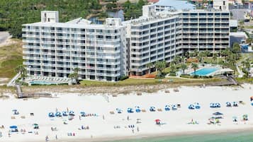 A beachfront hotel with multiple floors, a pool, and beach umbrellas.