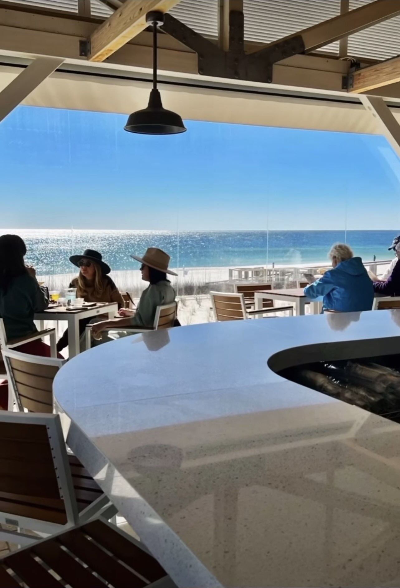 An outdoor dining area with a view of the ocean, tables, chairs, and a hanging light fixture.