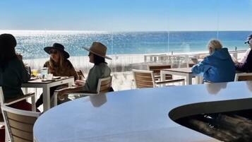 An outdoor dining area with a view of the ocean, tables, chairs, and a hanging light fixture.