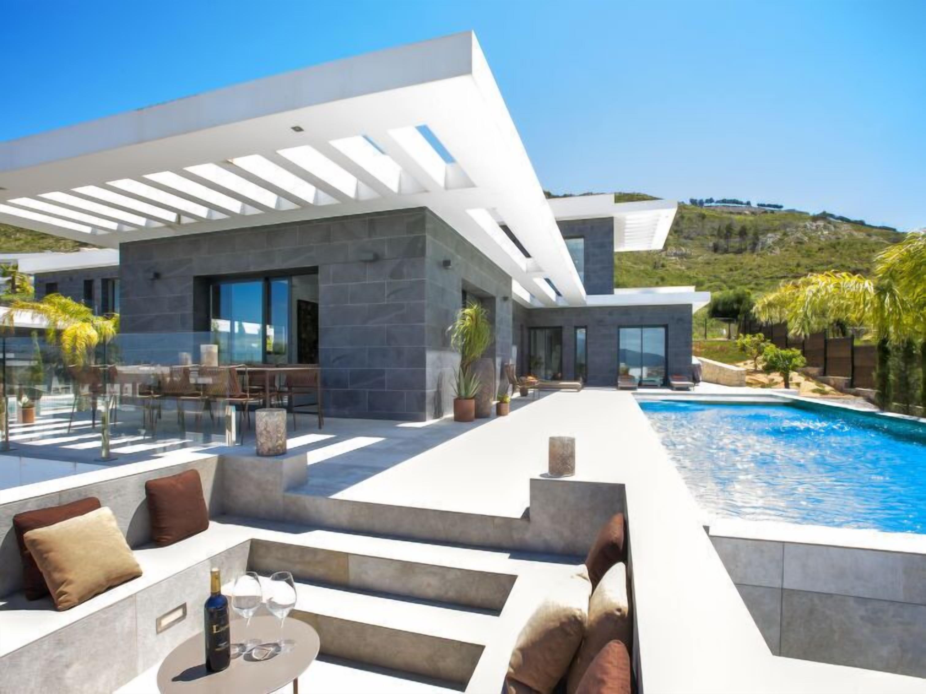 A modern house with a pool, outdoor seating, and a view of the hills.